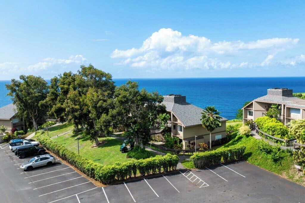 A coastal hotel with multiple-story buildings, parking, and a view of the ocean.