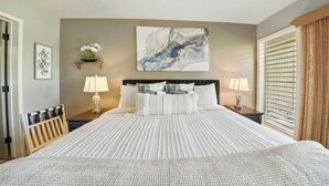 Un dormitorio con una cama grande, dos mesitas de noche con lámparas, una obra de arte en la pared y una ventana con persianas.