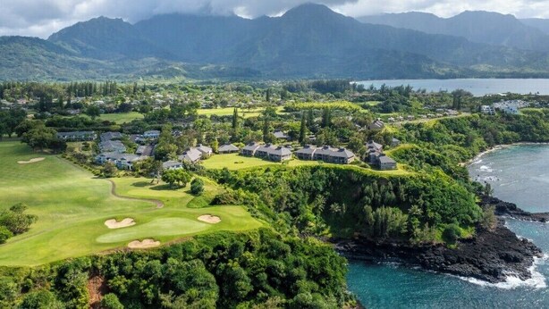 Un campo de golf con vistas al mar, rodeado de exuberante vegetación y edificios residenciales.