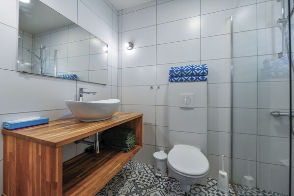 Een moderne badkamer met een houten wastafelmeubel, een witte wastafel en vloertegels met een patroon.