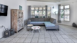 Ein Wohnzimmer mit grauem Sofa, einem weißen Couchtisch, einem Holzschrank und einem an der Wand befestigten Fernseher.