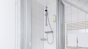 Une douche d’angle avec une porte en verre, des murs recouverts de carreaux blancs et un lavabo d’angle doté d’un porte-serviettes.