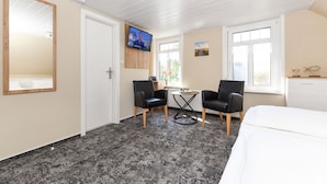 Une chambre d’hôtel avec un grand lit, deux chaises noires, une petite table ronde et un téléviseur fixé au mur.