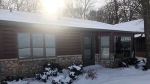 A log cabin with a stone foundation, large windows, and a snow-covered roof. - 30 steps to lake, Dock for fishing & swimming, Families Welcome!   (Miltona)