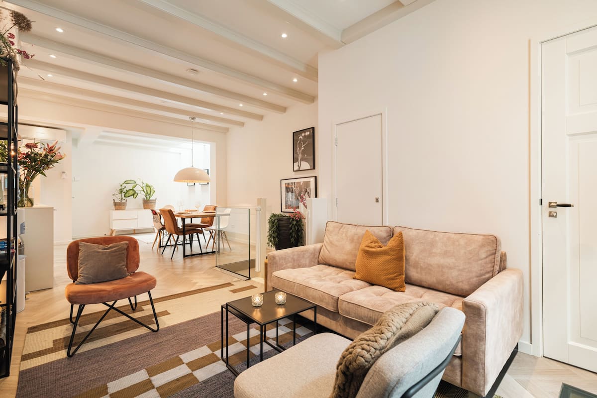Een moderne woonkamer met een bank, fauteuil en salontafel. Achtergrond toont een eethoek met een tafel en stoelen.