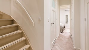 Un couloir avec un escalier, des murs blancs et un plancher en bois.