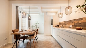 Une cuisine moderne avec un plancher en bois, un coin repas avec une table et des chaises en bois, et des luminaires suspendus.