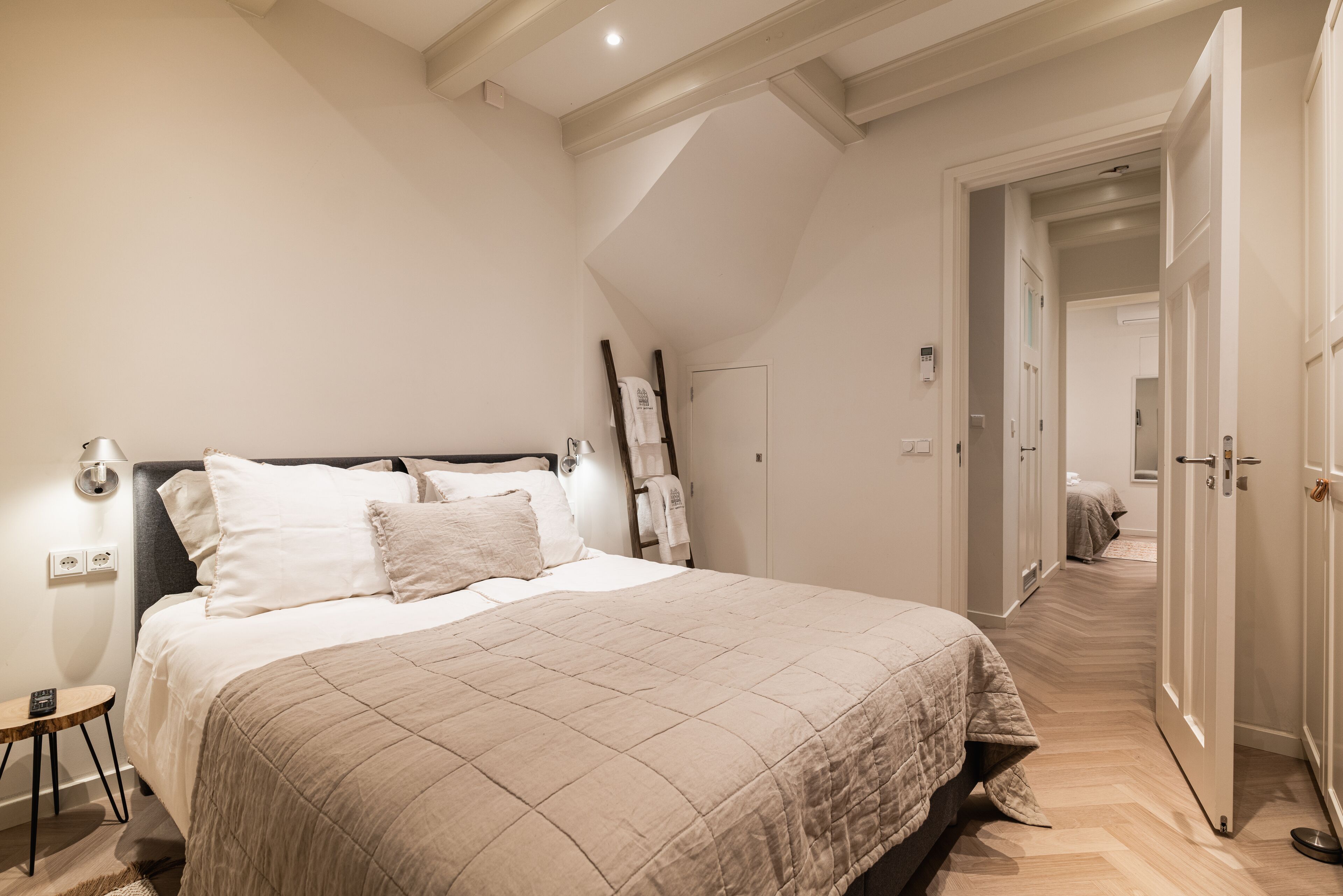 Una camera da letto con un letto grande, un comodino, una lampada e una scala in legno appoggiata al muro.