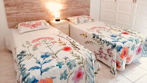 A bedroom with two beds, each with floral bedding, a bedside table with a lamp, and a wardrobe with a white door. - Americas II Holiday Home (Playa de las Américas)