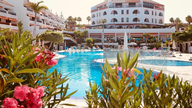 A pool area with lounge chairs and a building with multiple balconies in the background. - Americas II Holiday Home (Playa de las Américas)