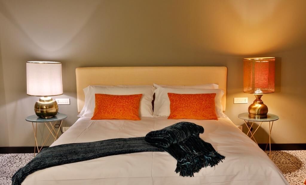 A hotel room with a bed, two pillows, a blanket, and two bedside lamps.