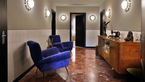 Un pasillo con dos sillones azules, un aparador de madera con adornos, y apliques en la pared.