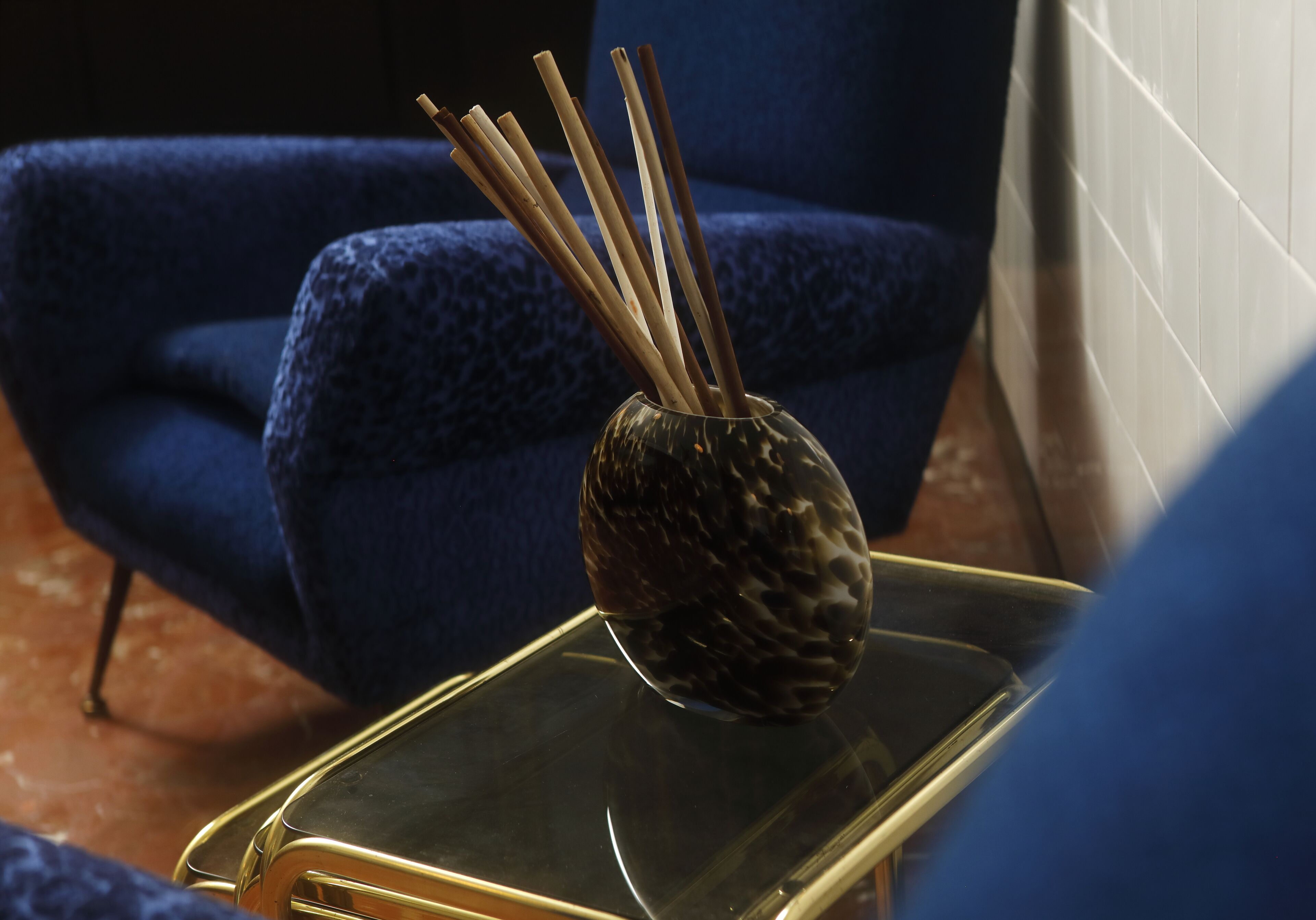 A smartphone on a glass table with a decorative vase containing reed sticks.