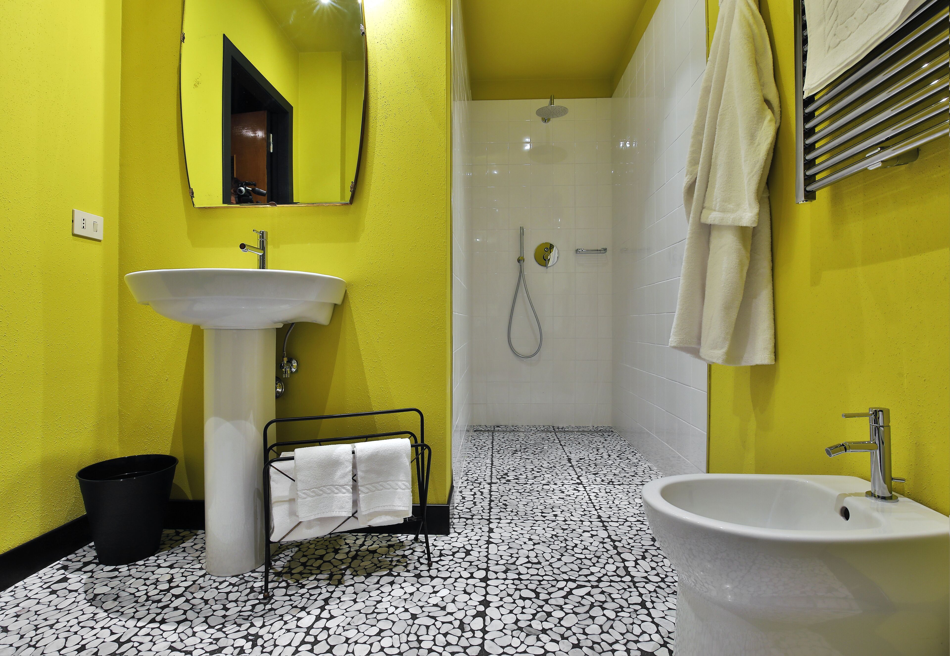 Un baño con un lavamanos blanco, un espejo, una ducha y un perchero para toallas.