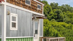 A rustic cabin with a front porch, a green exterior, and a shingled roof.