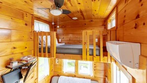 A cabin with a bed, a desk with a computer, a ceiling fan, and a window.
