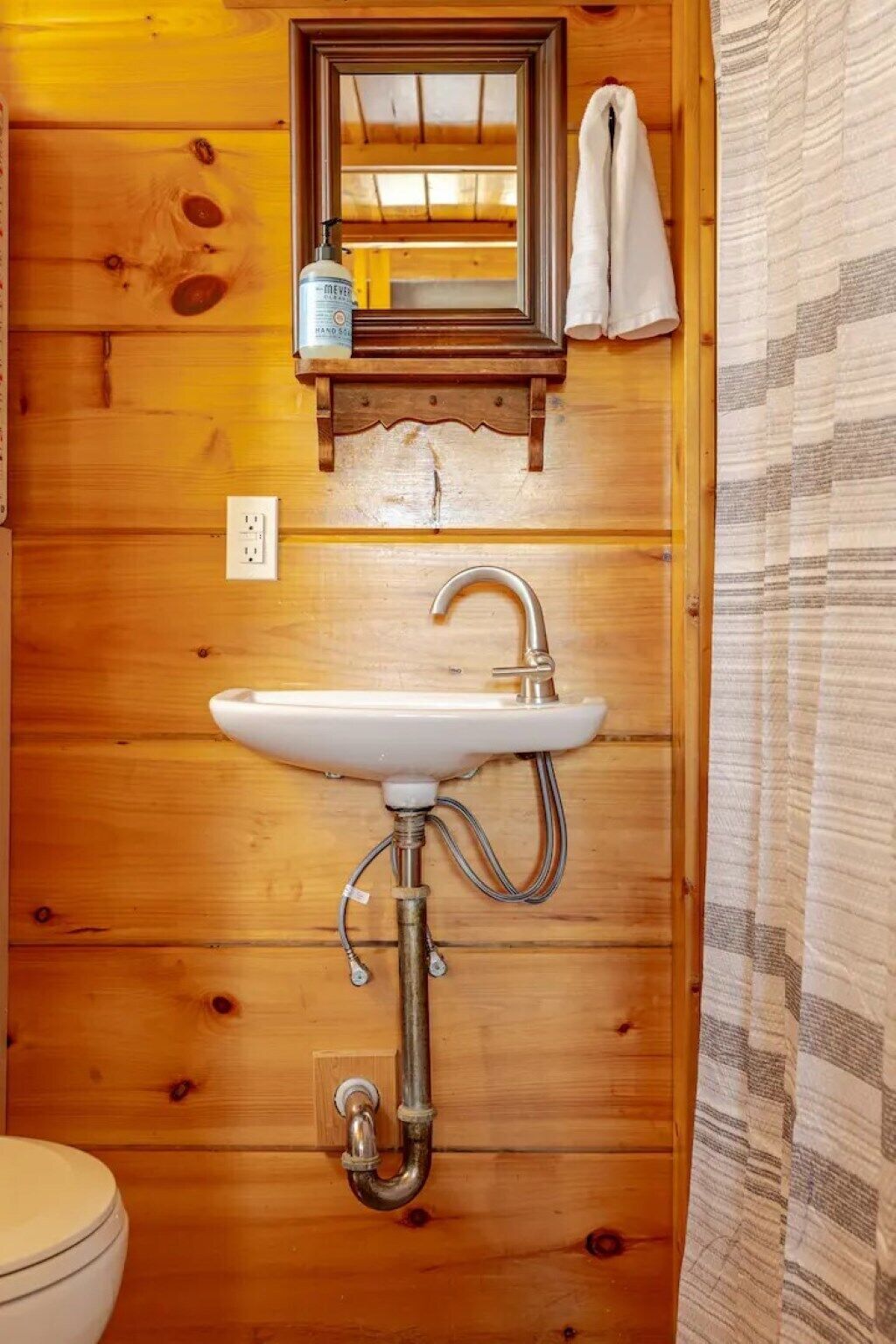 A wooden bathroom with a white sink, a mirror, and a towel hanging on the wall.