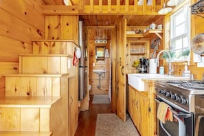 Interno di una baita in legno con angolo cottura, scala in legno e bagno a vista.
