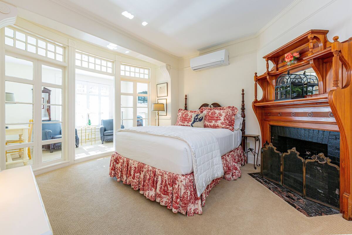 A bedroom with a large bed, a fireplace, and a view of the outside through large windows.