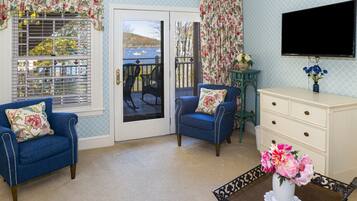 A room with a blue armchair, a white dresser, and a table with a vase of flowers.