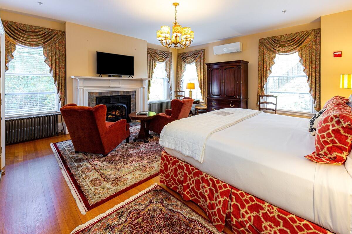 A hotel room with a large bed, a fireplace, a television, and a view of the city.