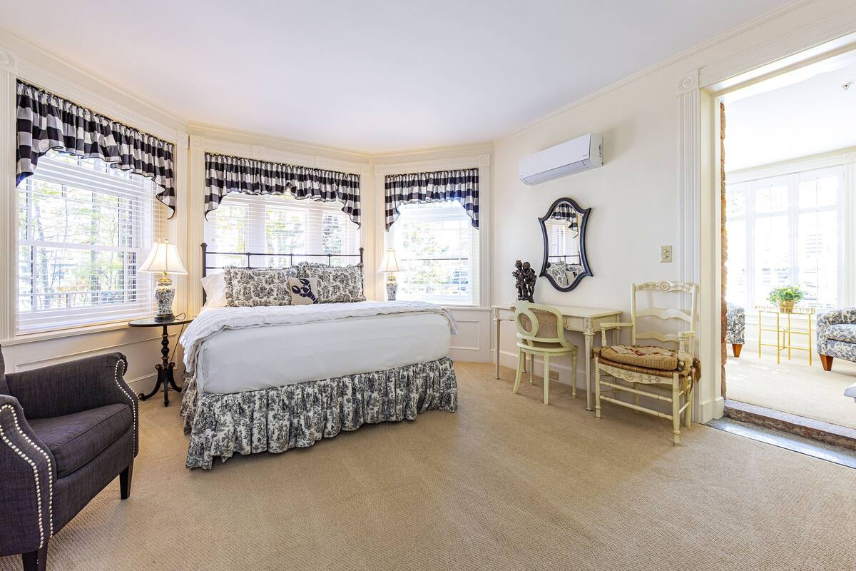 A bedroom with a large bed, two chairs, a small table, and a mirror.