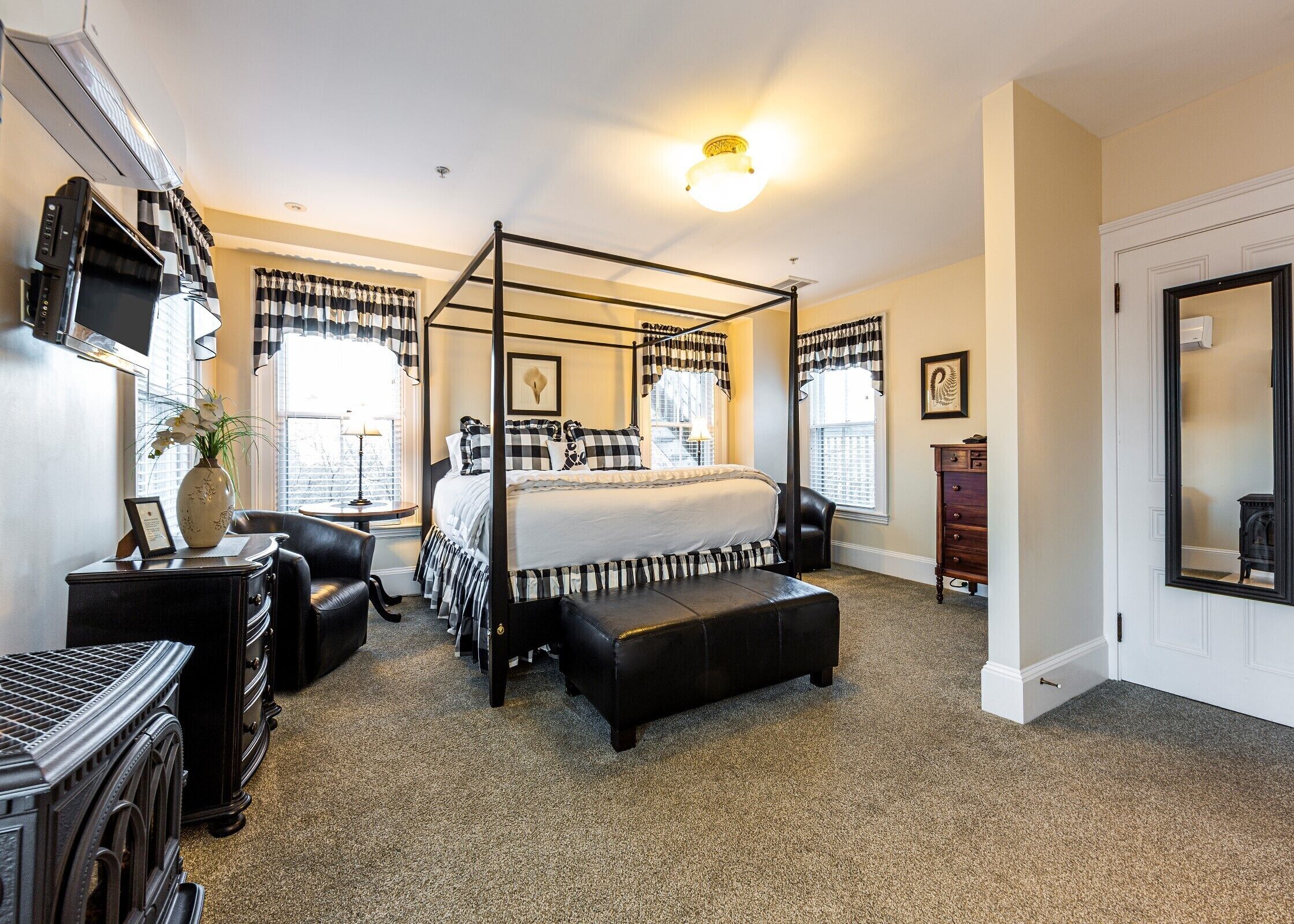 A four-poster bed with a black and white checkered bedspread, a bedside table with a lamp, and a dresser with a mirror.