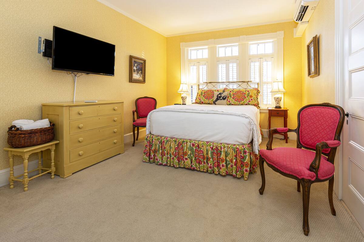 A hotel room with a bed, dresser, chairs, a television, and a window with curtains.