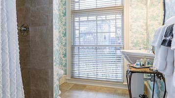 A bathroom with a shower, a vanity with a mirror, and a window with blinds.
