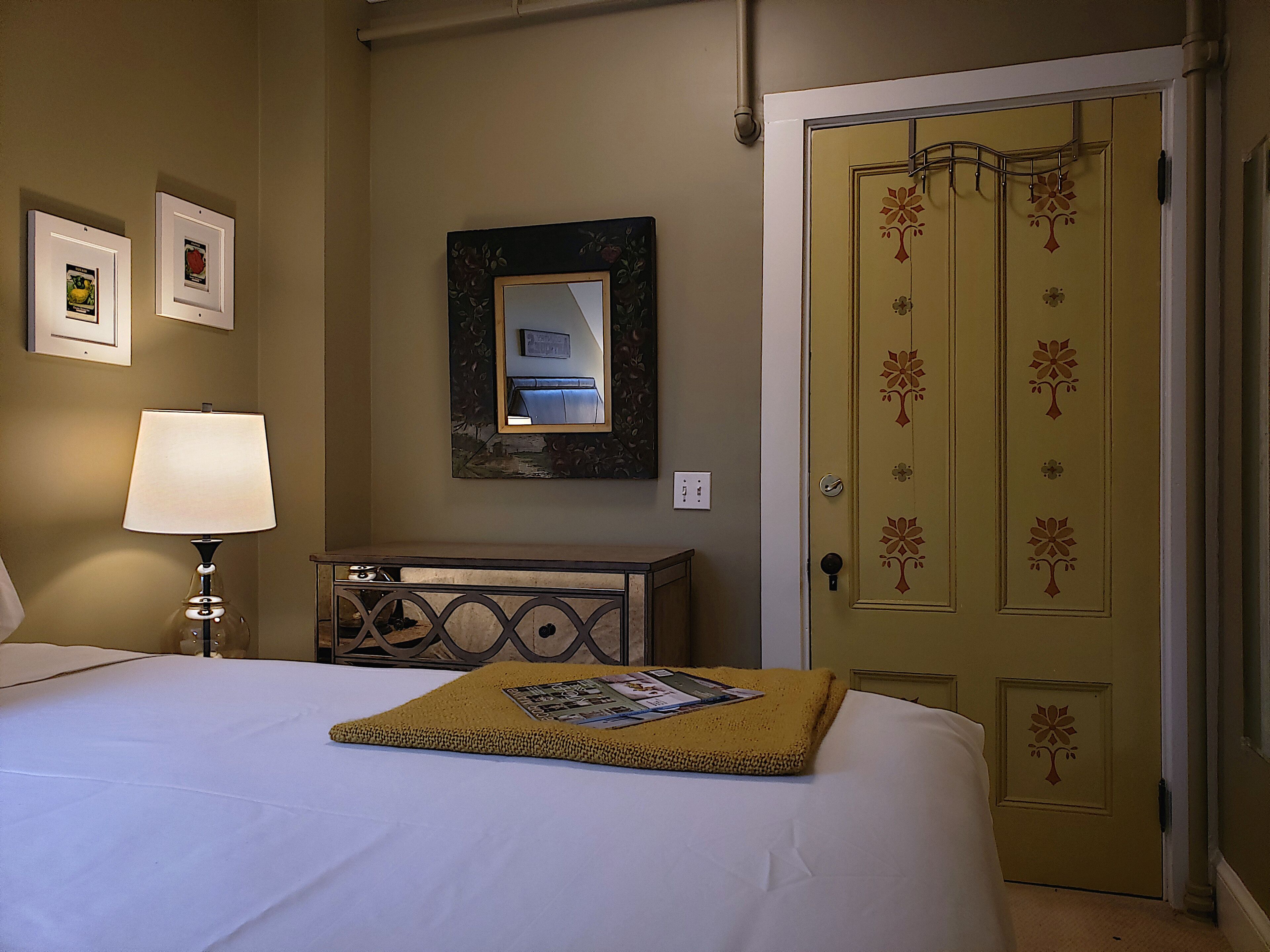 A hotel room with a bed, a bedside lamp, a dresser, a mirror, and a door with floral decorations.