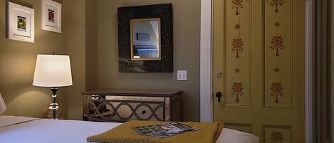 A hotel room with a bed, a bedside lamp, a dresser, a mirror, and a door with floral decorations.