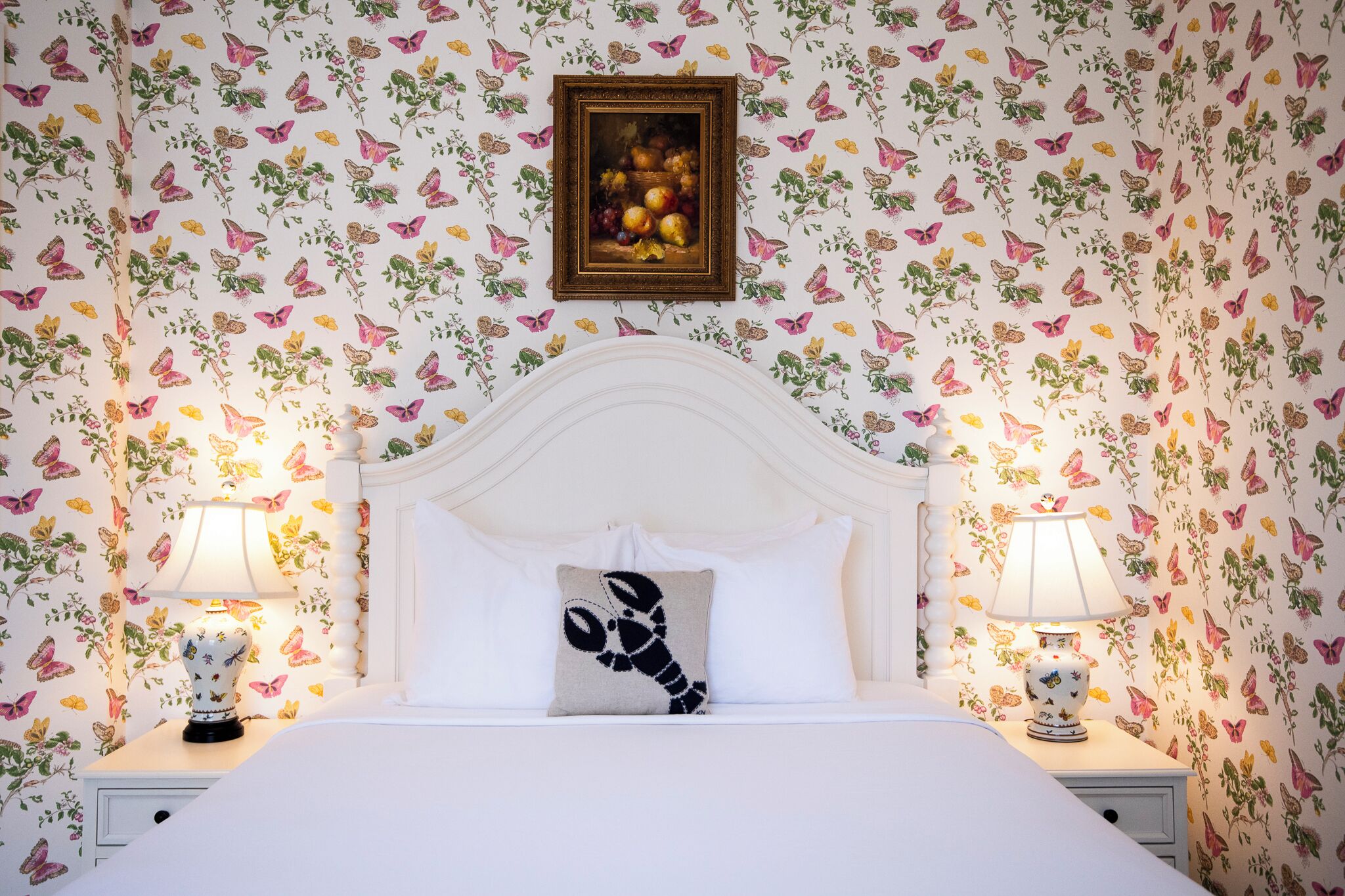 Une chambre à coucher avec un lit blanc, un tableau encadré au-dessus de la tête de lit et deux lampes de chevet.