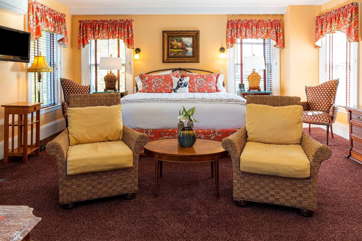 A hotel room with a large bed, two armchairs, a small table, and a TV.