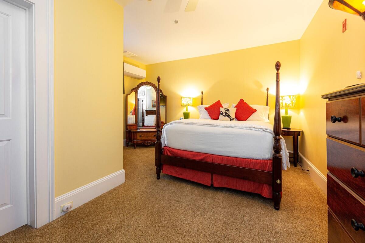 A bedroom with a four-poster bed, a wooden dresser, and a mirror.