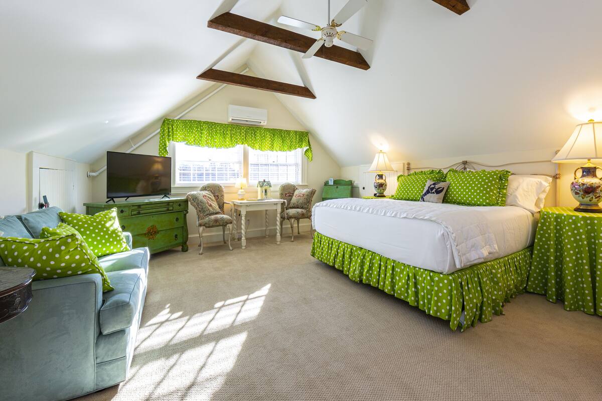 A cozy attic bedroom with a bed, a desk, and a TV.