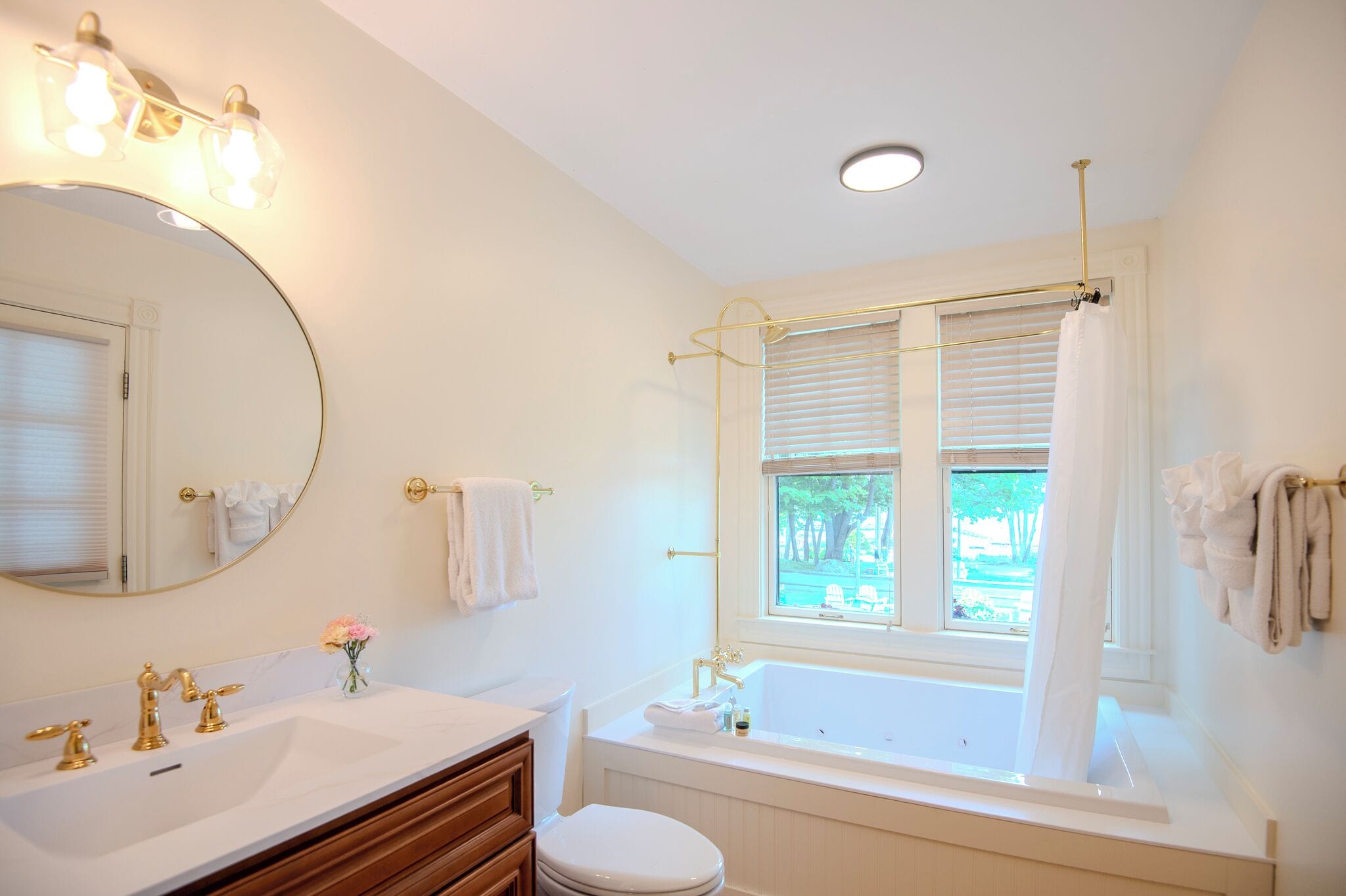 Un baño con lavamanos doble, bañera, inodoro, espejo y ventana con persianas.