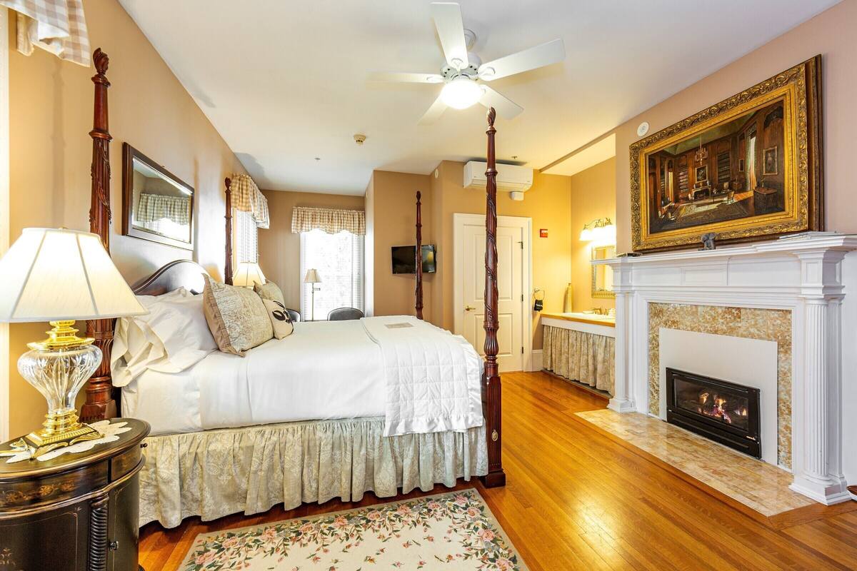 A bedroom with a four-poster bed, a fireplace, and a ceiling fan.