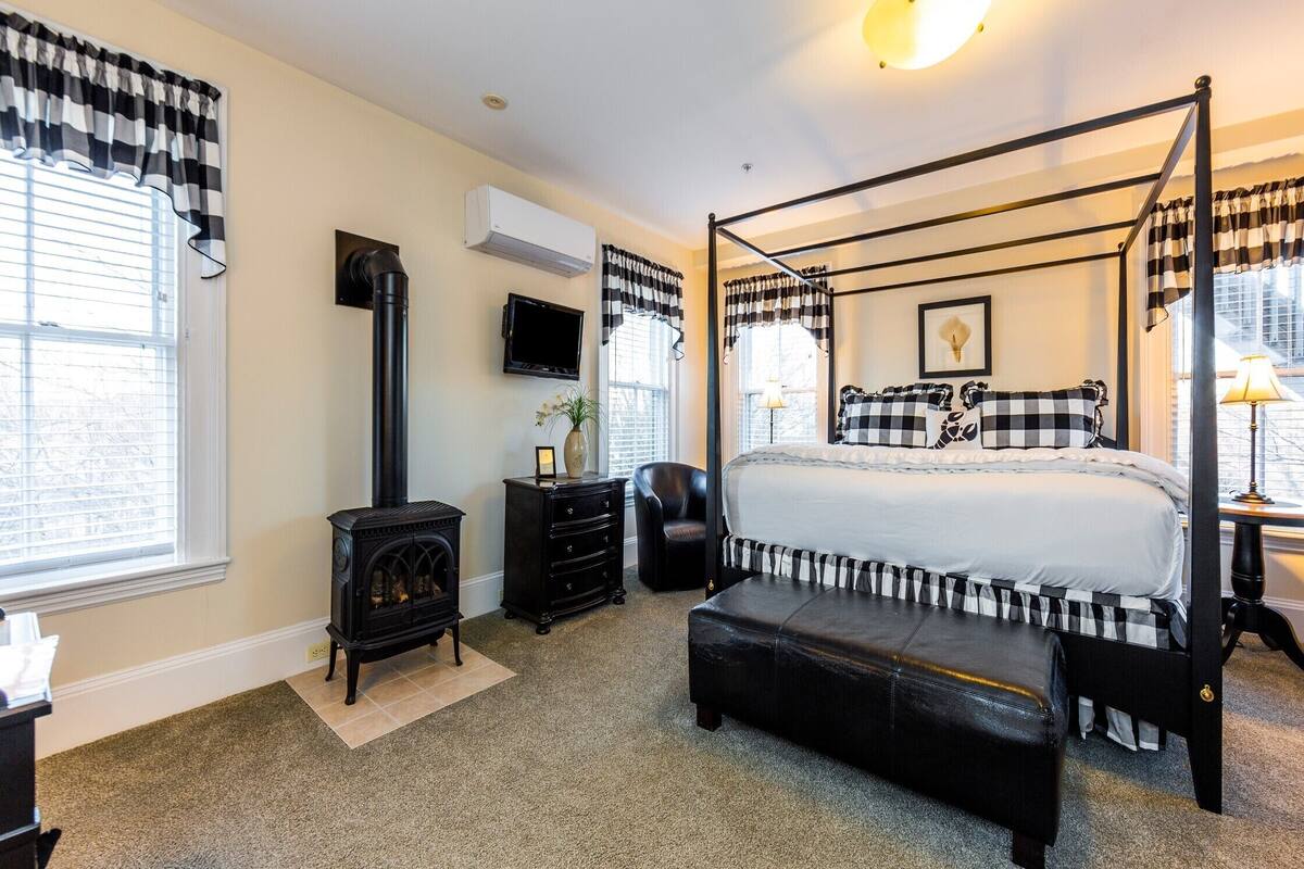 A bedroom with a four-poster bed, a fireplace, a TV, and a window with curtains.