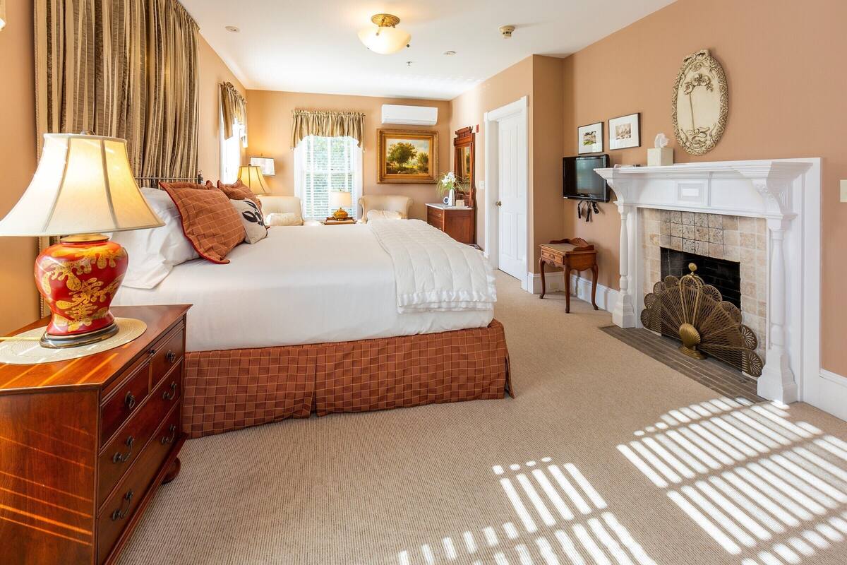 A hotel bedroom with a large bed, a dresser, a fireplace, and a television.