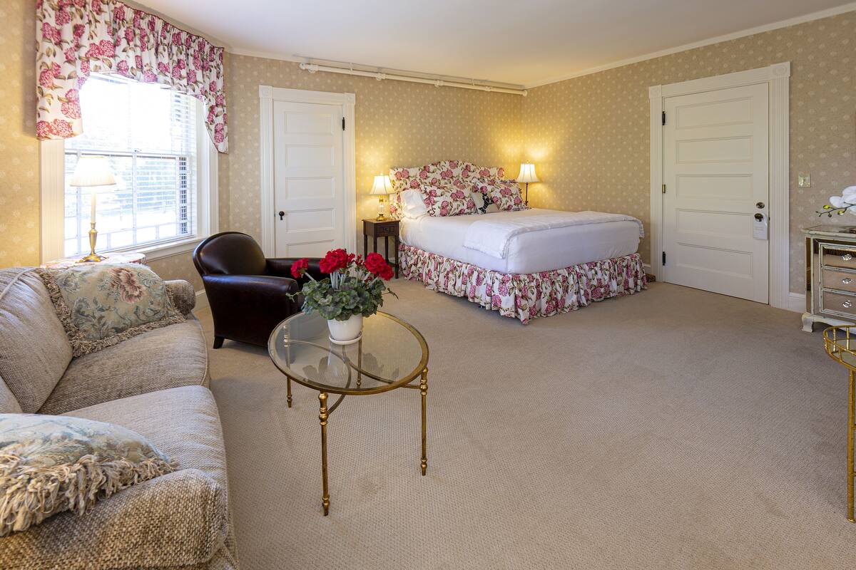 A bedroom with a bed, a chair, a table, and a window with curtains.