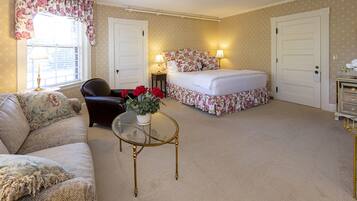 A bedroom with a bed, a chair, a table, and a window with curtains.
