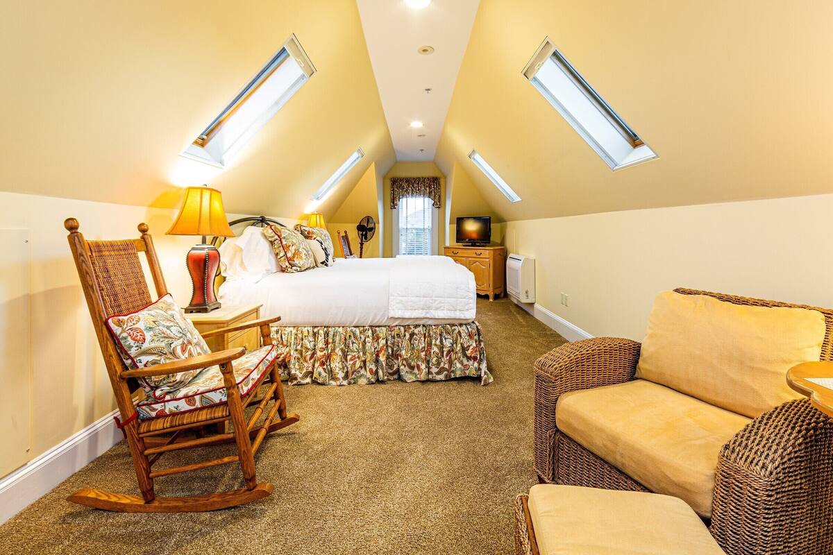 A cozy attic bedroom with a large bed, a rocking chair, a sofa, and a television.
