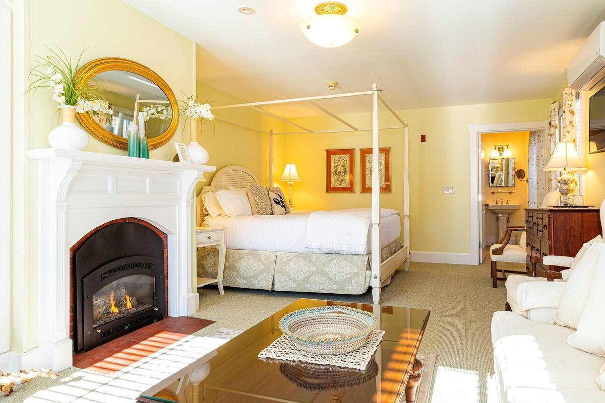 A bedroom with a four-poster bed, a fireplace, and a sitting area with a coffee table.