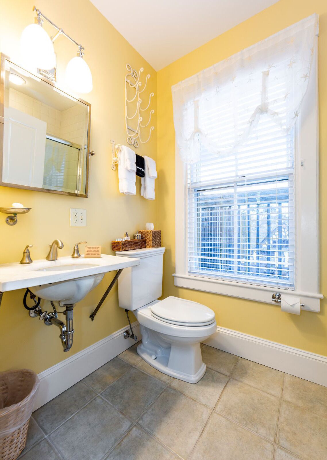 Een badkamer met een wit wastafelmeubel, toilet en raam met zonwering.