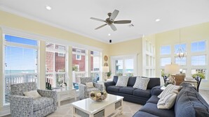 Un salon spacieux doté d’un ventilateur de plafond, de grandes fenêtres, d’un canapé bleu foncé, de fauteuils à motifs et d’une table basse agrémentée d’objets décoratifs.