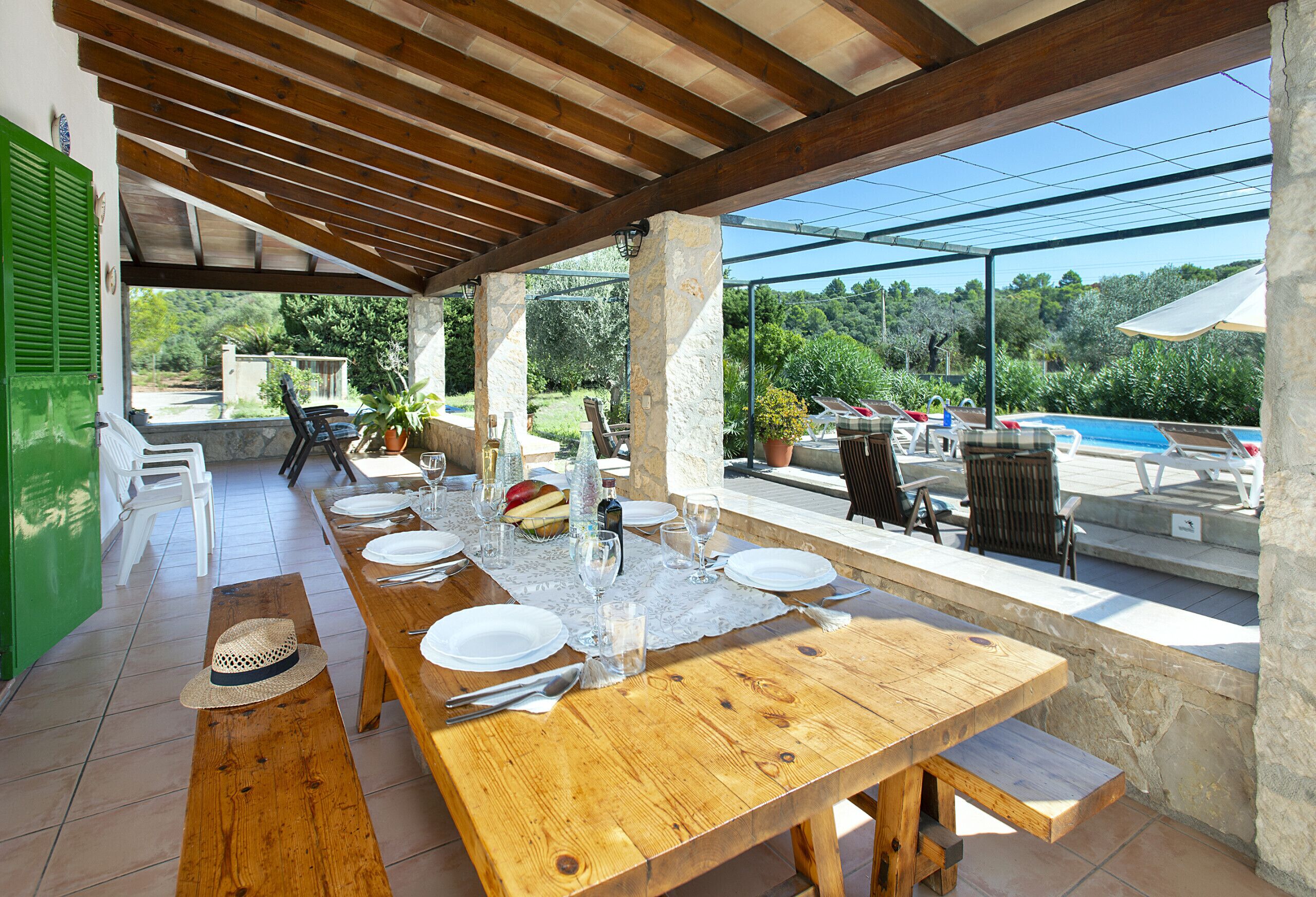 Ein Essbereich im Freien mit einem Holztisch, gedeckt für sechs Personen, umgeben von Steinpfeilern und mit Blick auf Pool und Garten.