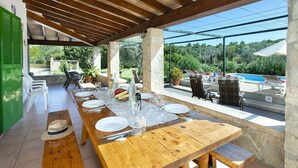 An outdoor dining area with a wooden table set for six, surrounded by stone pillars, and overlooking a pool and garden. - VILLA FINQUITA - RUSTIC STAY (Puerto Pollensa)
