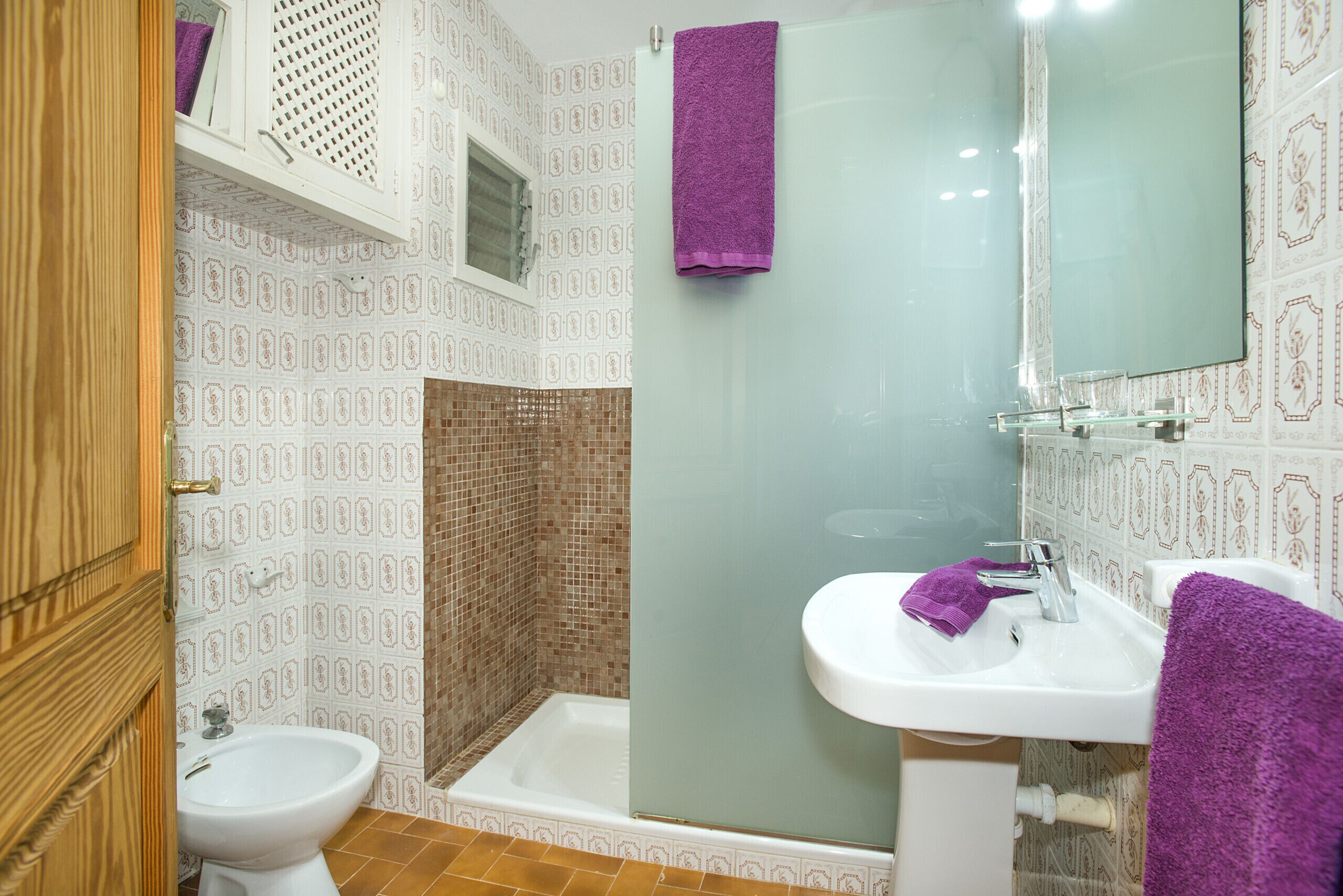 A bathroom with patterned wallpaper, a white sink, a mirror, and a shower enclosure.