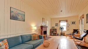 Tunnelmallinen olohuone, jossa on sininen sohva, takka, kirjahylly ja tuuletin.