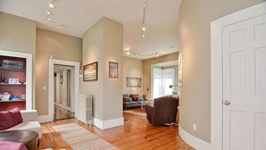 A spacious living room with a wooden floor, a sofa, a coffee table, and a fireplace. There is a door leading to another room and a window with blinds.